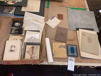 Lot overview with various vintage and antique photographs packed in a cardboard box and several loose mounted portraits and albums laid out on a table.