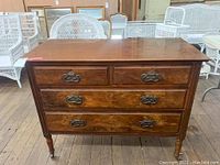 Front view of a vintage wooden dresser showing four drawers with dark metal handles, surface with scratches, standing on caster wheels.