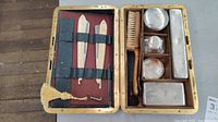 Inside of antique leather grooming case showing razors, brush, metal containers, and glass bottle arranged neatly in compartmentalized interior.