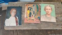 Three vintage oil on canvas portraits displayed on a wooden surface.