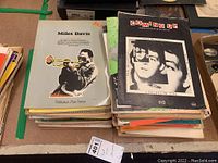 Two stacks of vintage sheet music and songbooks with varied designs including a Miles Davis cover and 'Coming Up' songbook.