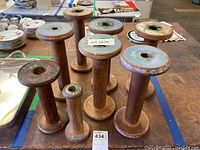 Front view of 8 wooden weaving loom spools with some blue paint on top and one spool noticeably missing top disc.