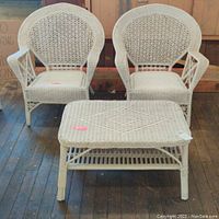 Front view of two white wicker chairs with rounded backs and matching wicker table with diamond pattern top.