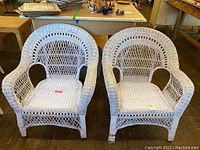 Front view of two matching white wicker chairs showing detailed woven design and curved arms, placed indoors.