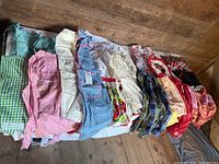 Photo of vintage aprons and housecoats laid out showing various colors and patterns including gingham, floral, denim, and patchwork fabrics.