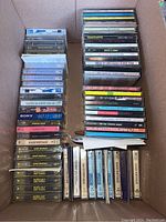 Photo of multiple audio cassette tapes stacked neatly in a box, some sealed in plastic wrapping.