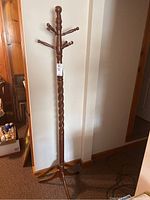 Full view of wooden coat tree stand showing twisted central post, eight hooks and tripod base, with visible scratches on feet and arms