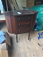 Front view of Cowan wooden sewing cabinet showing the three dovetail drawers, legs, and closed lift-top side compartments.