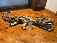Full view of driftwood alligator sculpture on wooden floor with a water bottle for scale