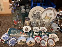 Photo showing blue glass mason jars, souvenir mini plates, glassware, mugs, and the RMS Queen Mary pennant in background