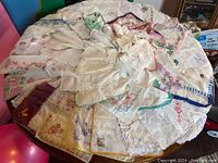 Sixty handkerchiefs spread on table showing varied colors, floral patterns, and lace edges.
