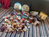 Large assortment of vintage matchbooks with multiple decorative tins placed behind on a woven blanket