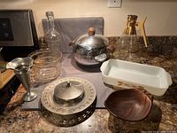 Overall view of all items in the lot on countertop including ice buckets, decanter, trays, casserole dish, and vase.