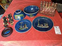 Full lot overview showing two turquoise plates, two bowls, figural clay sailboat sculpture, Peruvian whistle, and textile straps arranged on a red tablecloth