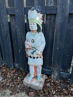 Full frontal view of the painted cement Native American sculpture showing full body and feathered headdress.