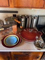 Overview of lot showing red enameled cast iron pot, nesting pans, popcorn popper, food mill, four stainless steel canisters with wooden knobs, and Nordic Ware cookie tool box.