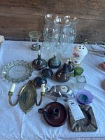 Full lot of unused pottery lamps, candle holders, glass hurricane lamp shades, ashtrays and potpourri burners displayed on white cloth with rustic wooden background.