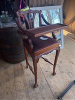 Front angle view of the ornate carved wooden high chair with velvety seat and attached wooden tray showing overall condition and craftsmanship.