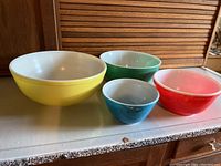 Front view of four vintage Pyrex nesting bowls in yellow, green, red, and blue showing size range and colors