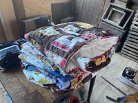 Set of five folded quilts stacked on a table showing a variety of fabrics and textures.