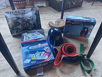 Various items including boxed Halo Mega Bloks toy set, ThinkFun Laser Maze and Circuit Maze games, Newton Microscope in box, plastic ball helmet, karate belts, and a vintage ball mitt.
