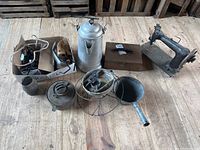Lot overview including sewing machine, kettle, lock box, irons, lantern base, and additional tools on wooden surface.