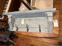 Top view of painted wooden wall shelf with three dark metal hooks and decorative carved ends.