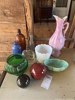 Lot overview showing four vintage bottles, three planters, a pink ceramic pitcher, and two decorative balls on a wooden surface.