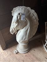 Front angled view of the large hollow composite horse head sculpture on pedestal with detached ears on floor.