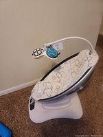 Side angle of the 4moms MamaRoo 4 baby swing showing the seat with patterned cushion and hanging soft toys on mobile arm.