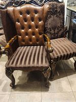 Front view of armchair showing tufted faux leather back, carved wood arms and striped fabric seat