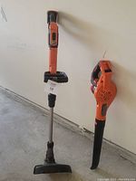 Two BLACK+DECKER cordless tools side by side against a wall: a leaf blower and a string trimmer with battery.