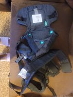 Photo of baby carrier laid out flat showing fabric, strap, and snap buttons