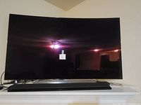 Front view of curved TV on white shelf with black soundbar beneath