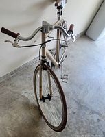 Front view of the beige Mongoose 700c bicycle showing curved handlebar with brown grips, front wheel, and brake cable.