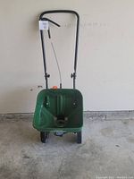 Front view of green Scotts Turf Builder EdgeGuard Mini broadcast spreader with black handle and wheels on concrete floor.