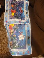 Two splash tummy time tummy mats laid on a brown surface, showing the colorful underwater design and floating shapes inside the water section.