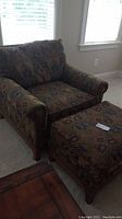 Front view of upholstered armchair with matching ottoman, fabric pattern visible, wood legs shown.