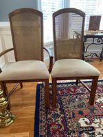 Two pecan dining chairs, one with arms and one armless, showing cane backs and upholstered seats. Light scratches visible on wood frames.