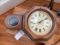 Full view of Verichron clock with wooden octagonal frame and pendulum section placed on cardboard.