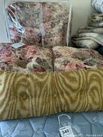 Floral comforter, matching shams, and long mustard-colored decorative pillow visible stacked on a bed.