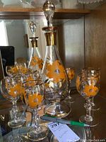 Full view of two decanters and six cognac glasses, showing orange floral hand painted details and gold trimming.