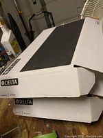 Two white boxes stacked with Delta brand labels visible, indicating contents are Delta faucets.