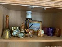 Shelf with various decorative items: brass bell, cricket box, carved wood rhinoceros, split geode stones, onyx candle holder, metal candle holder with candle