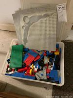 White plastic bin filled with assorted LEGO bricks and two large grey baseplates with terrain features on top
