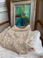Framed abstract painting behind crocheted scarf and table cloths on a chair