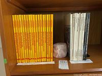 Photo showing 18 yellow Kodak Library of Creative Photography volumes on a wooden shelf alongside white and black spine books and a stone candle holder not included in the lot.