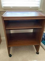Front view of wooden printer table showing top, middle cubby shelf, bottom shelf, legs with casters