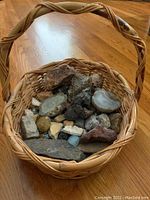 Wide view of basket containing assorted rocks and marbles on wooden floor.