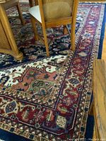 Close-up showing corner of navy blue rug with detailed floral and geometric multicolor patterns, and white fringes on the edge.